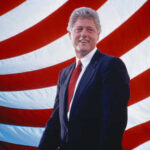 Bill Clinton smiling in front of an American flag