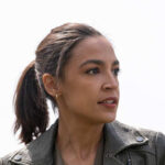 A woman with a ponytail wearing a leather jacket, looking thoughtfully into the distance