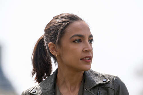 A woman with a ponytail wearing a leather jacket, looking thoughtfully into the distance