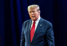 Man in dark suit and red tie speaking