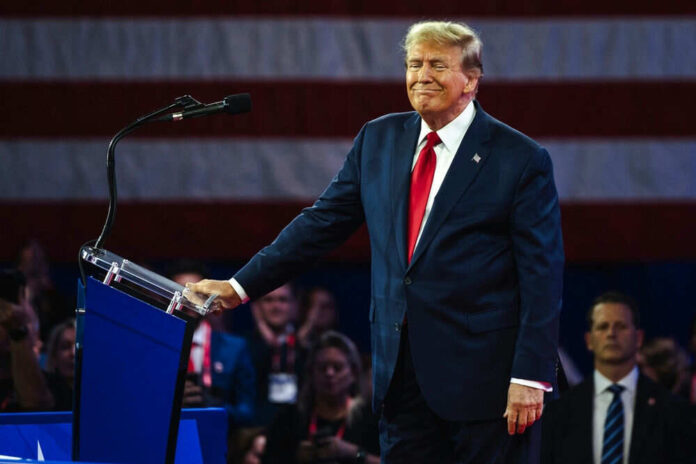 Man in suit at podium with American flag backdrop