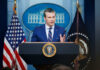 Man speaking at podium with US flags behind