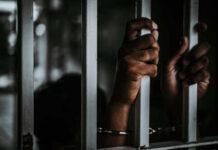 Hands gripping prison bars, suggesting confinement