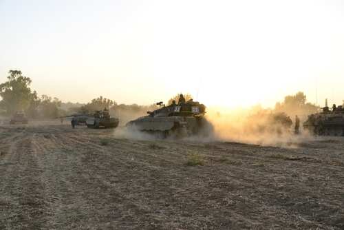 Military tanks moving through a dusty field at sunset