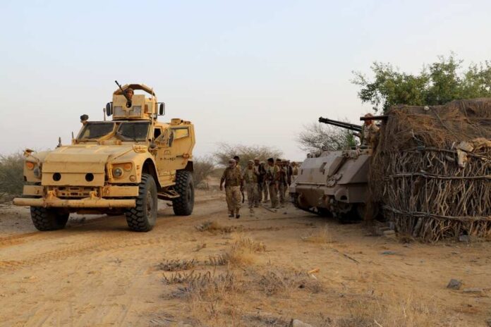 Military personnel walking near armored vehicles in a desert setting