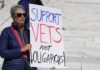 Woman holding a sign that reads 'Support Vets Not Oligarchs!'