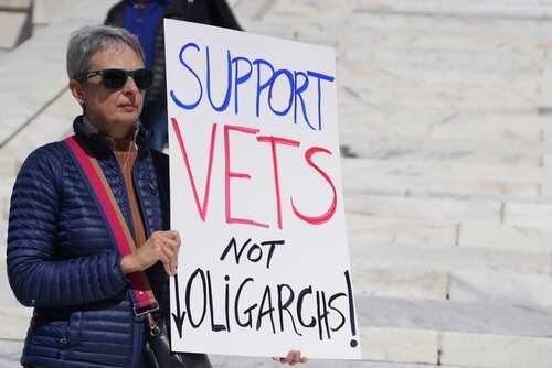 Woman holding a sign that reads 'Support Vets Not Oligarchs!'
