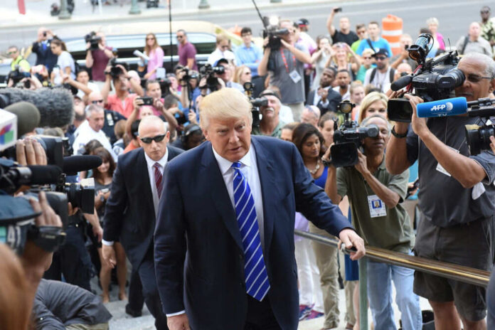 Man in suit surrounded by media and cameras