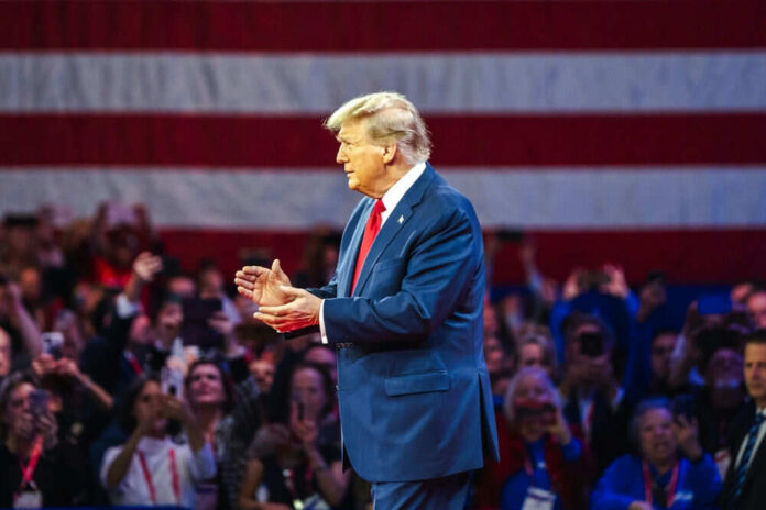 2434408273 Man in blue suit gesturing with American flag background