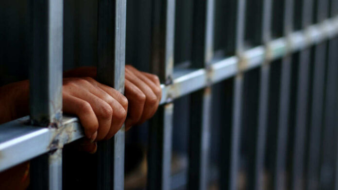 Hands gripping metal prison bars tightly
