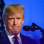Man speaking at a podium with flag background