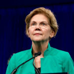 Warren’s Latest Trump Attack Sparks Ethics Backfire Person speaking at podium wearing green jacket