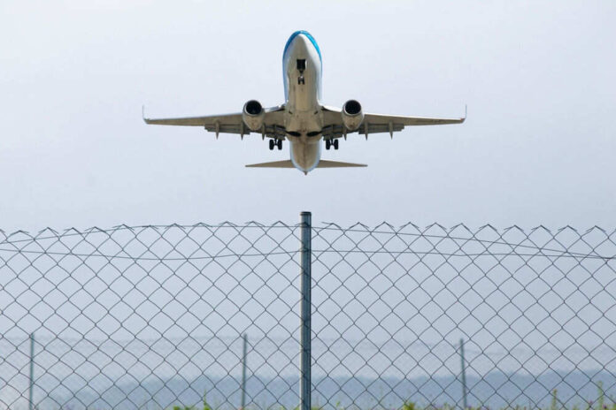 Airplane taking off above a wire fence