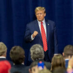 Trump’s Tariff Threat Forces Pharma SURRENDER Man in suit addressing crowd with phones raised