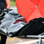 Person carrying body bag on stretcher outdoors