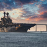 Missile Strikes or Narcotics Ops? The Debate Aircraft carrier near bridge under colorful sunset sky