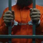 Murderer’s Shocking Plea: “I’d Do It Again” A prisoner in an orange jumpsuit holding jail bars with handcuffs