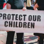 Person holding sign reading Protect Our Children