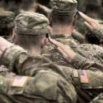 Soldiers in camouflage uniforms saluting with American flags