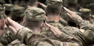 Soldiers in camouflage uniforms saluting with American flags