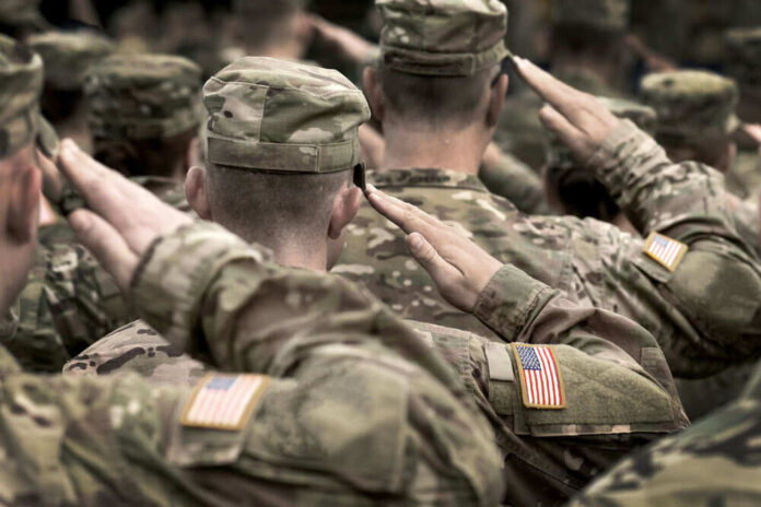 Soldiers in camouflage uniforms saluting with American flags