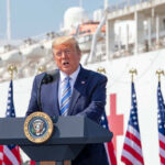 Man speaking at podium with flag background