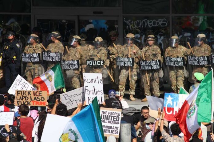 Protesters holding signs and flags in front of a line of National Guard members