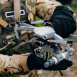 Person holding drone in camouflage uniform and gloves